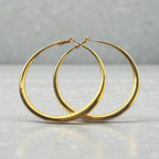 Représentation des grandes créoles dorées à l'or fin 24 carats sur fond sutudio gris