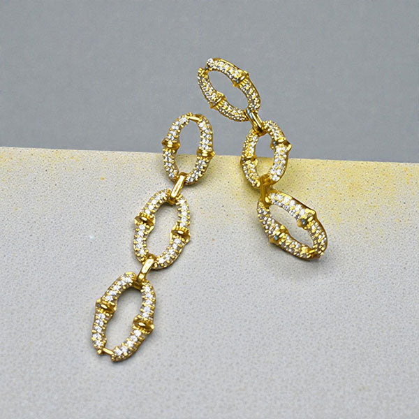 Représentation des boucles pendantes dorées à l'or fin 24 carats Secure sur fond studio gris