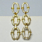 Représentation des boucles pendantes Secure dorées à l'or fin 24 carats sur fond studio gris